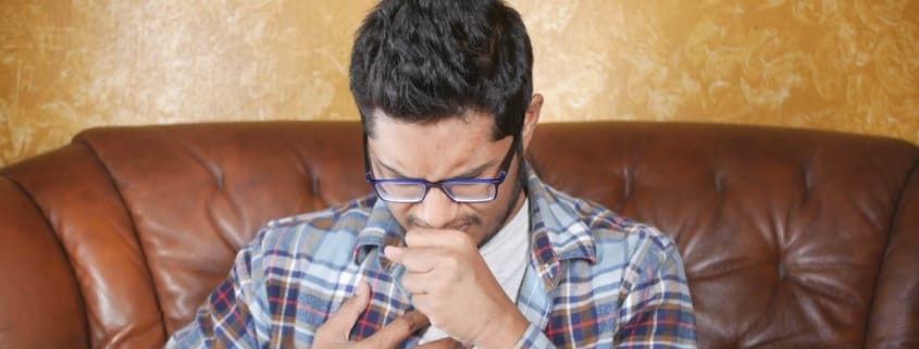 Person coughing into their hand from the effects and dangers of a cracked heat exchanger.