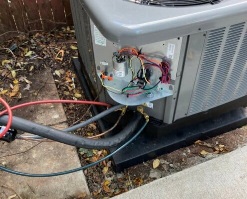 Air conditioning unit under repair with exposed wiring and connected refrigerant hoses.
