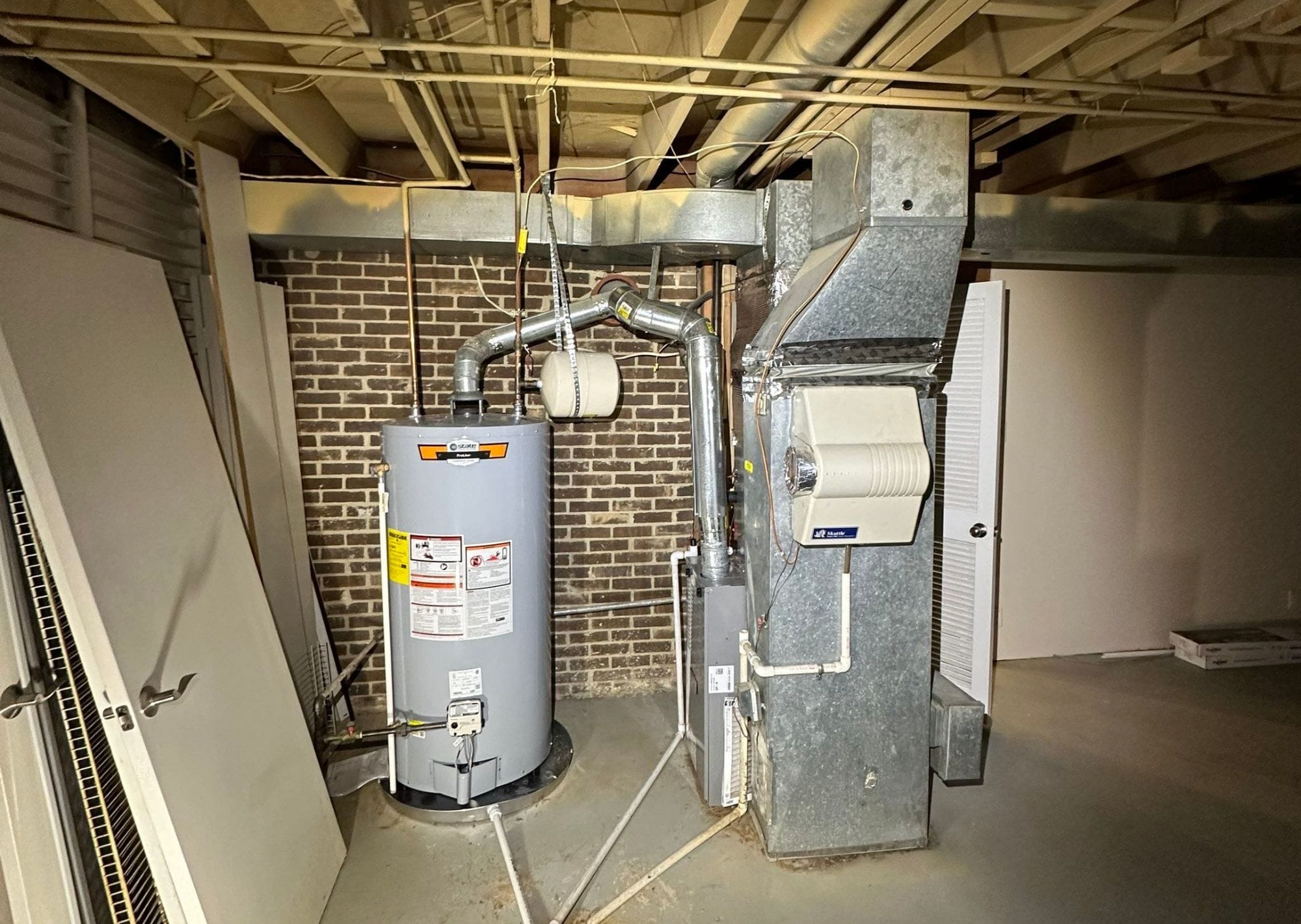 Basement water heater and furnace with exposed ceiling pipes.