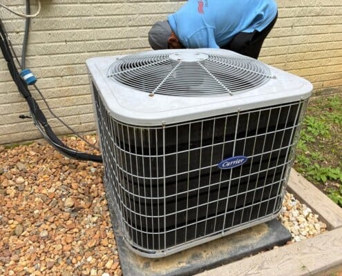Technician inspecting a Carrier air conditioning unit beside a brick wall.