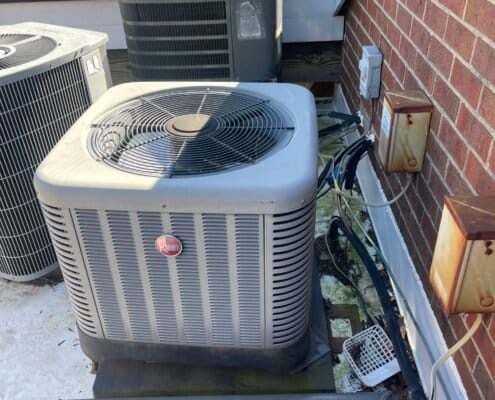 Three outdoor Rheem air conditioning units installed beside a brick wall.