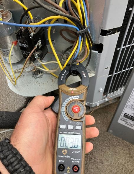 HVAC technician testing an AC unit with a clamp meter for Briggs in Ashburn, VA